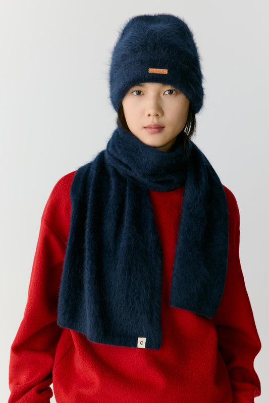 Portrait view of a woman wearing a navy blue cashmere scarf layered over a vibrant red top. The image highlights the plush texture, soft volume and fluid drape of the cashmere, while the deep navy shade creates a strong contrast that emphasizes the richness and depth of the material.