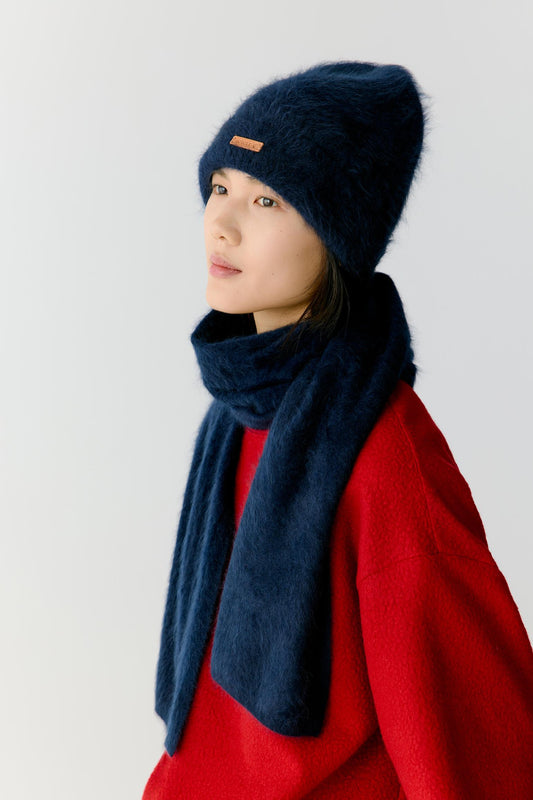 Portrait view of a woman wearing a navy blue cashmere beanie styled with a matching scarf. The image highlights the plush texture, soft volume and gently rounded shape of the beanie, while the deep navy shade emphasizes the richness and depth of the cashmere knit.