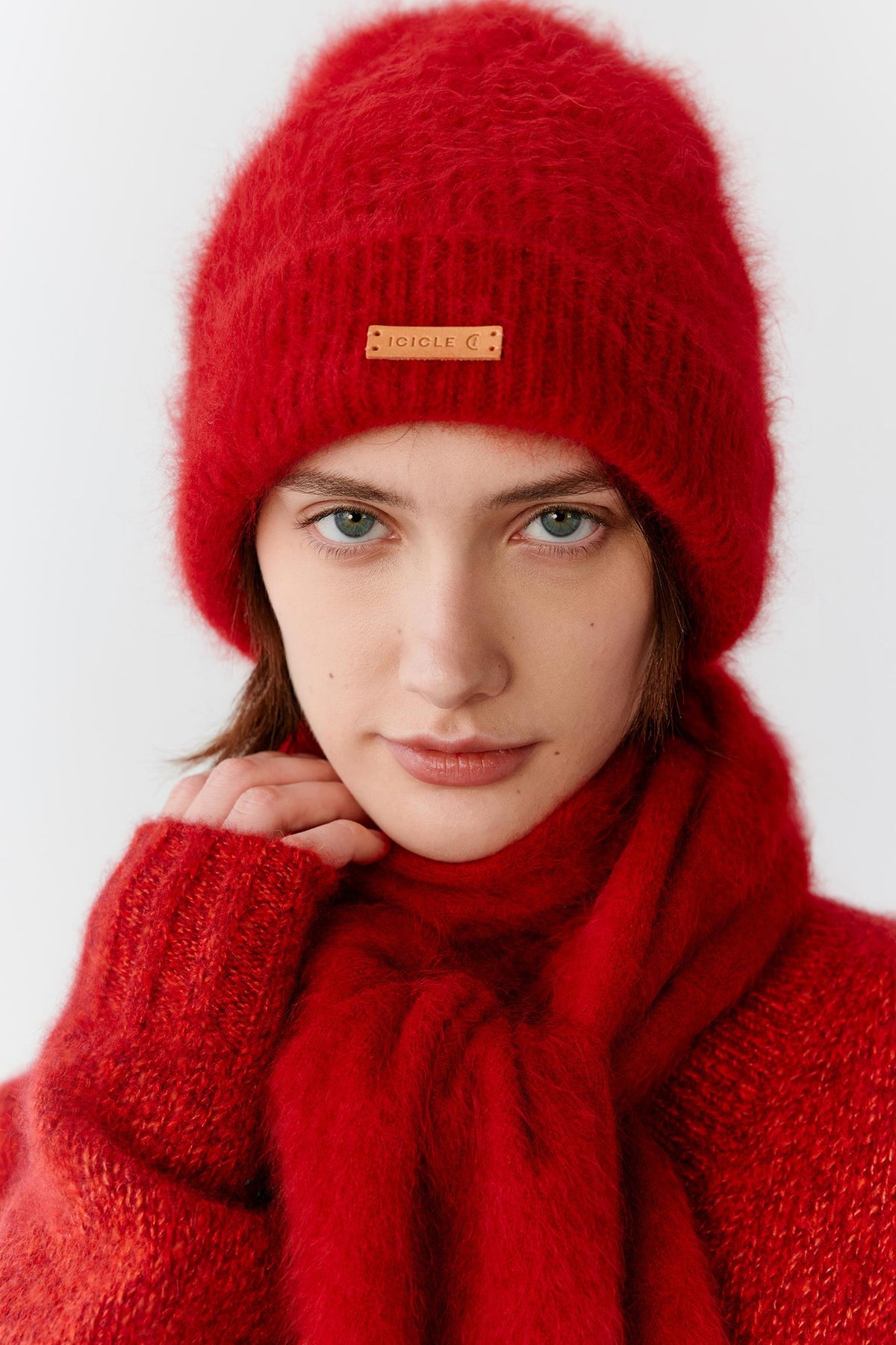 Portrait view of a woman wearing a deep red cashmere beanie styled with a matching scarf. The image highlights the plush texture, soft volume and fluffy surface of the cashmere knit, while the saturated red shade emphasizes the richness and depth of the material. A folded brim and contrasting front label complete the design.
