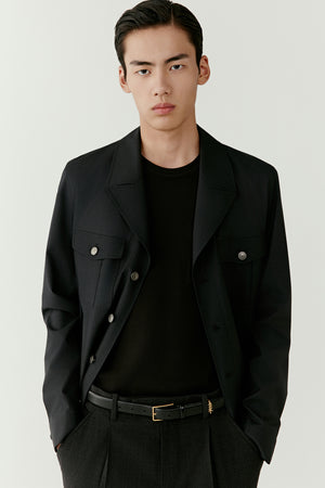 Portrait view of a man wearing a deep charcoal grey DEW wool and silk jacket with straight cut, highlighting the structured collar and clean lines.