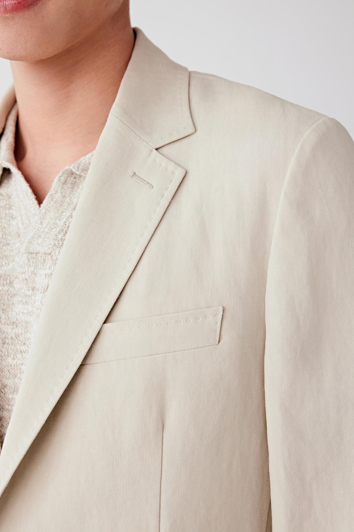 Close-up of the lapel and chest, detailing the notched lapel construction, button closure and the fine texture of the twisted linen yarn, with a matte surface and visible grain adding depth to the beige shade