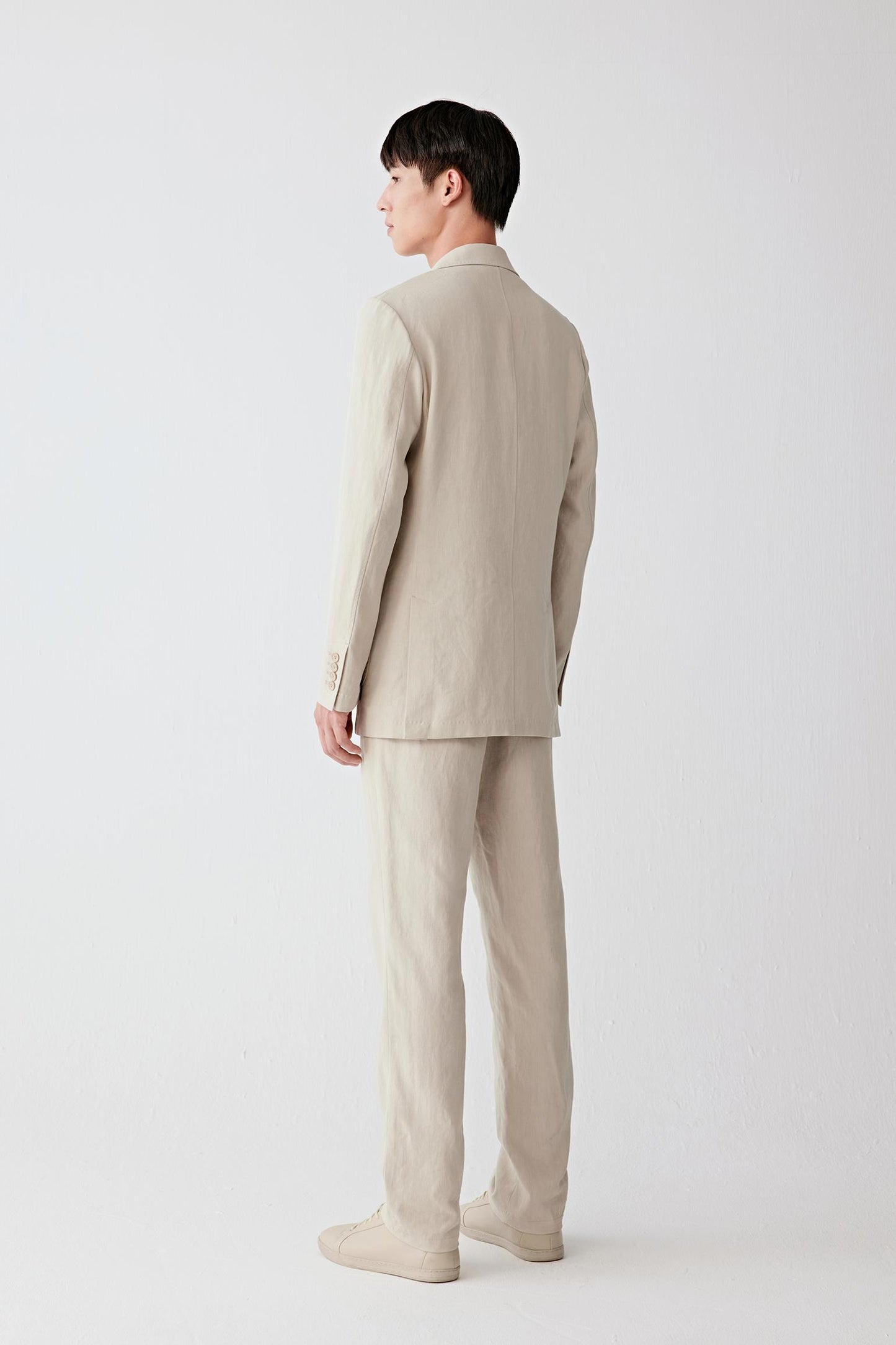 Full-length back view showing the rear silhouette, highlighting the structured shoulders, straight cut and continuous fall from collar to hem, with the fabric maintaining a breathable yet slightly crisp structure