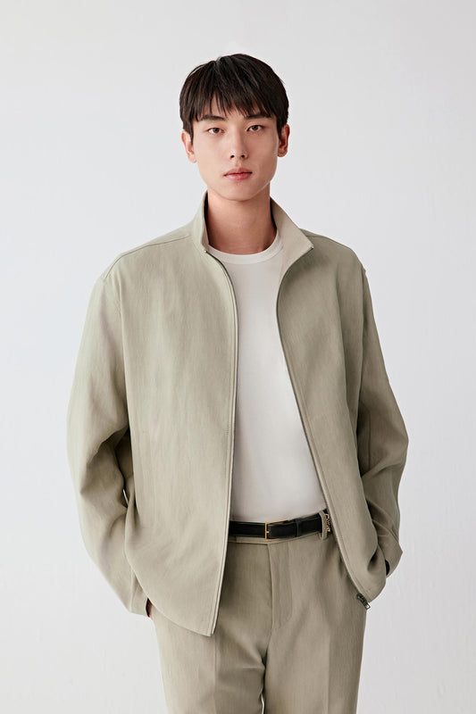 Three-quarter front view focusing on the upper body, emphasizing the stand collar, zip fastening and clean front construction, with the natural beige tone revealing depth and variation in the fabric texture