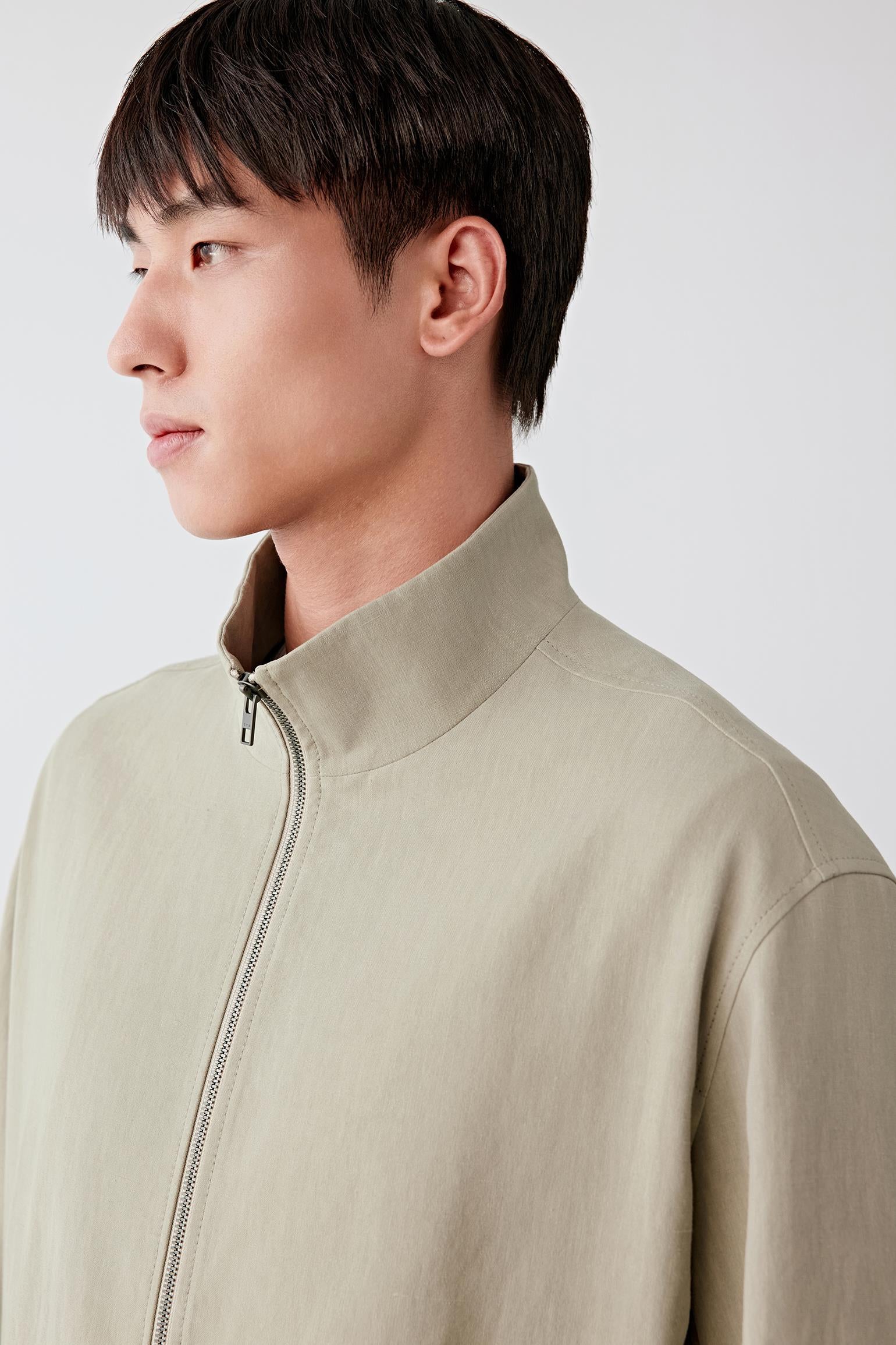 Close-up portrait focusing on the neckline and collar, detailing the stand collar construction, zip closure and fine linen weave, with a matte surface and visible natural grain