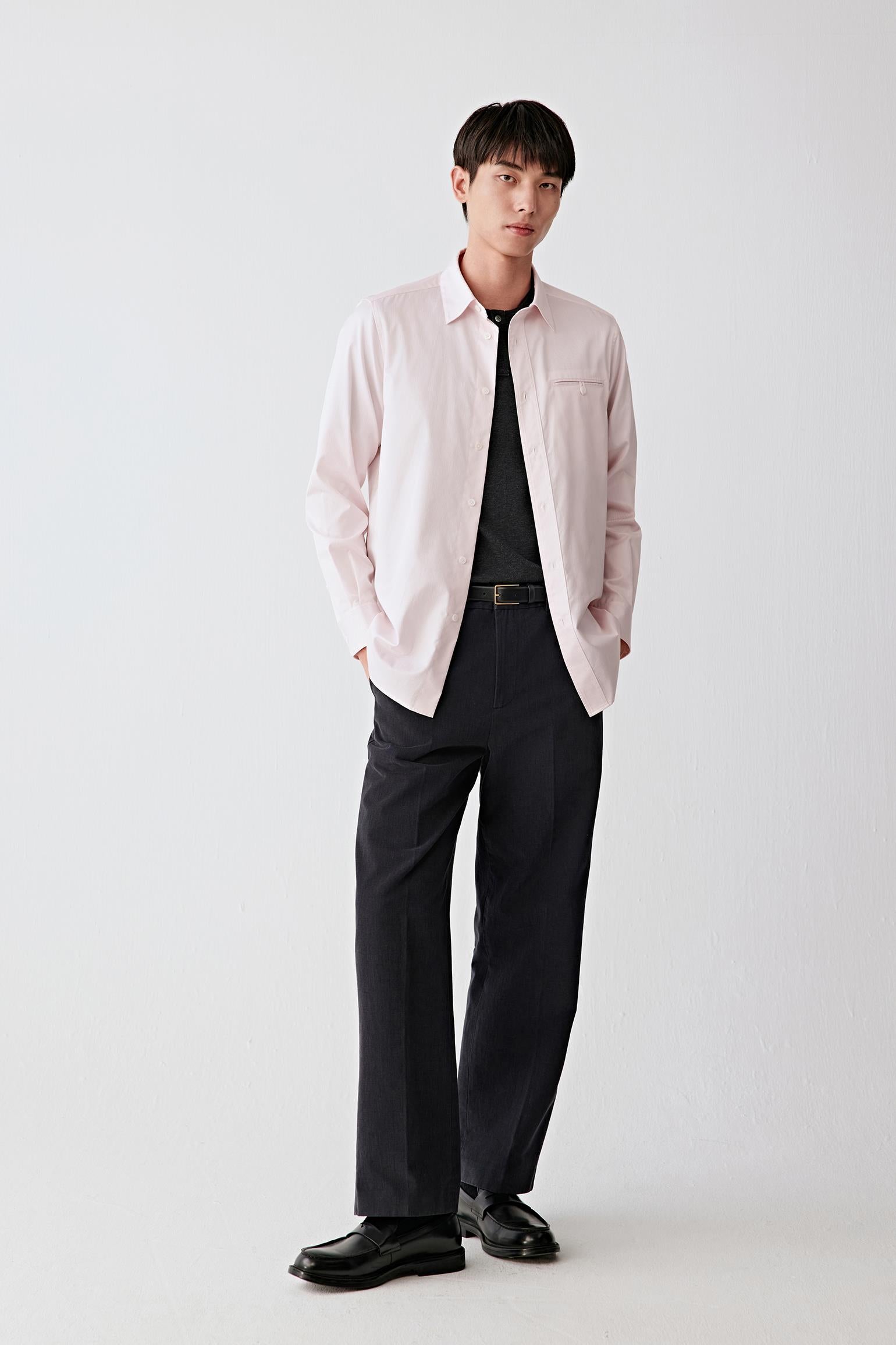 Full-length front view of a men’s light pink and white striped cotton twill shirt worn open over a dark T-shirt with black trousers.