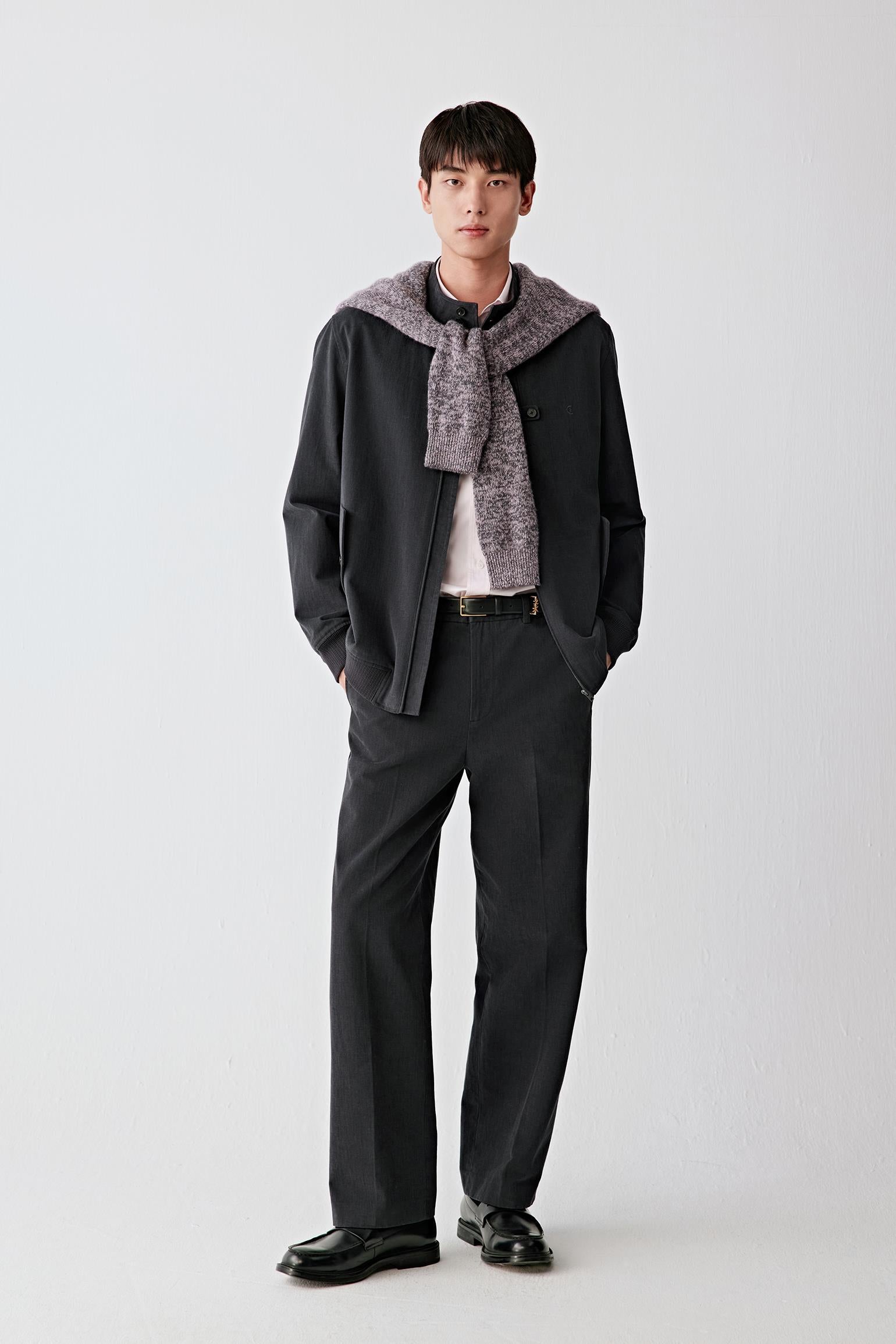 Full-length front view of a men’s black cotton twill jacket with zip fastening, worn over a light T-shirt and dark trousers.