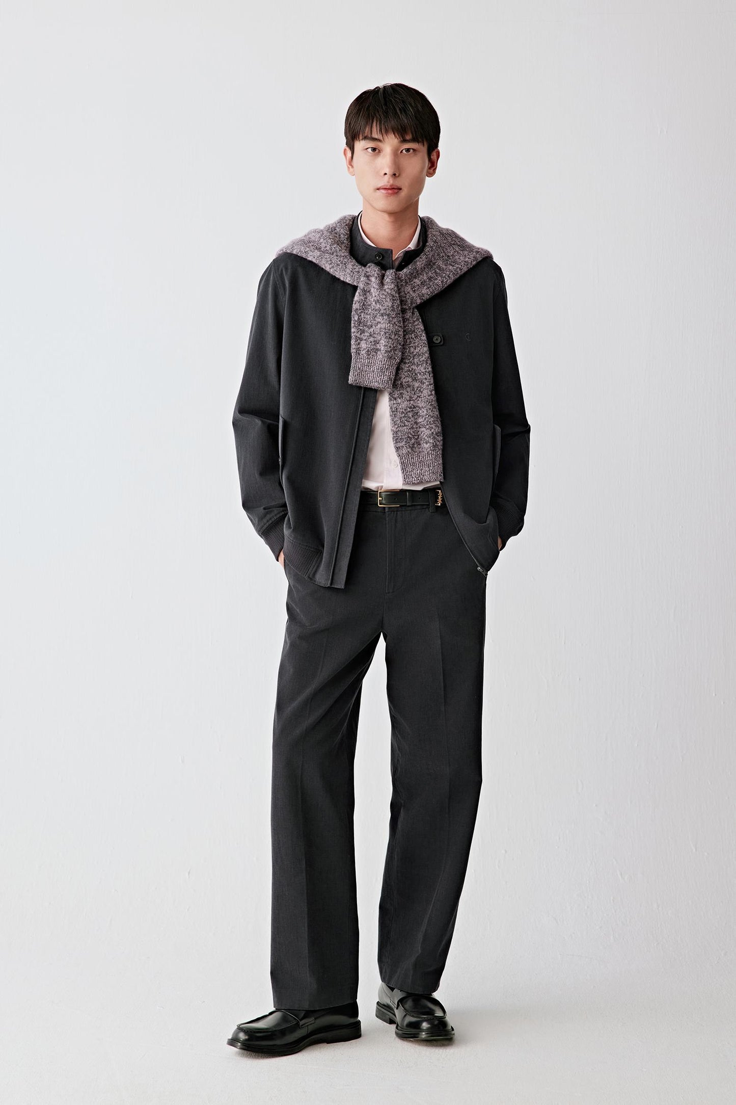 Man wearing black cotton twill trousers with a straight, relaxed fit, styled with a matching jacket, shirt and tie; full-length front view showing the clean lines, soft structure and slightly matte surface of the fabric.