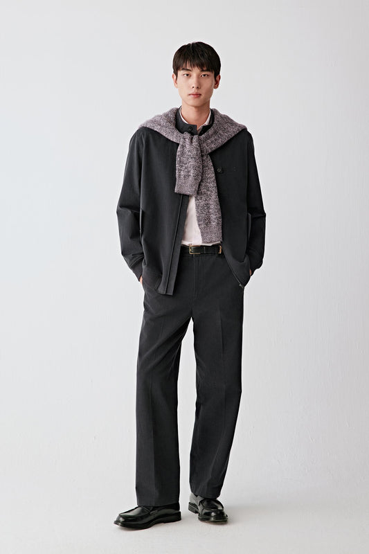 Man wearing black cotton twill trousers with a straight, relaxed fit, styled with a matching jacket, shirt and tie; full-length front view showing the clean lines, soft structure and slightly matte surface of the fabric.