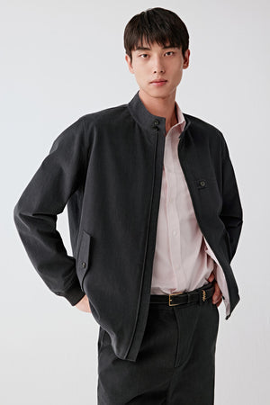 Man wearing a black cotton twill jacket with straight relaxed cut, styled with black trousers and light shirt, three-quarter front view.