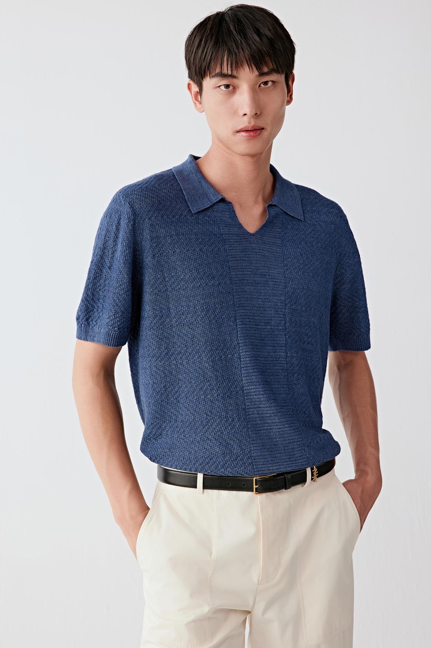 Three-quarter front view of a man wearing a blue linen yarn pullover, highlighting the relaxed silhouette, short sleeves and soft V-neckline, with a dry, textured surface and subtle tonal variation typical of linen knit