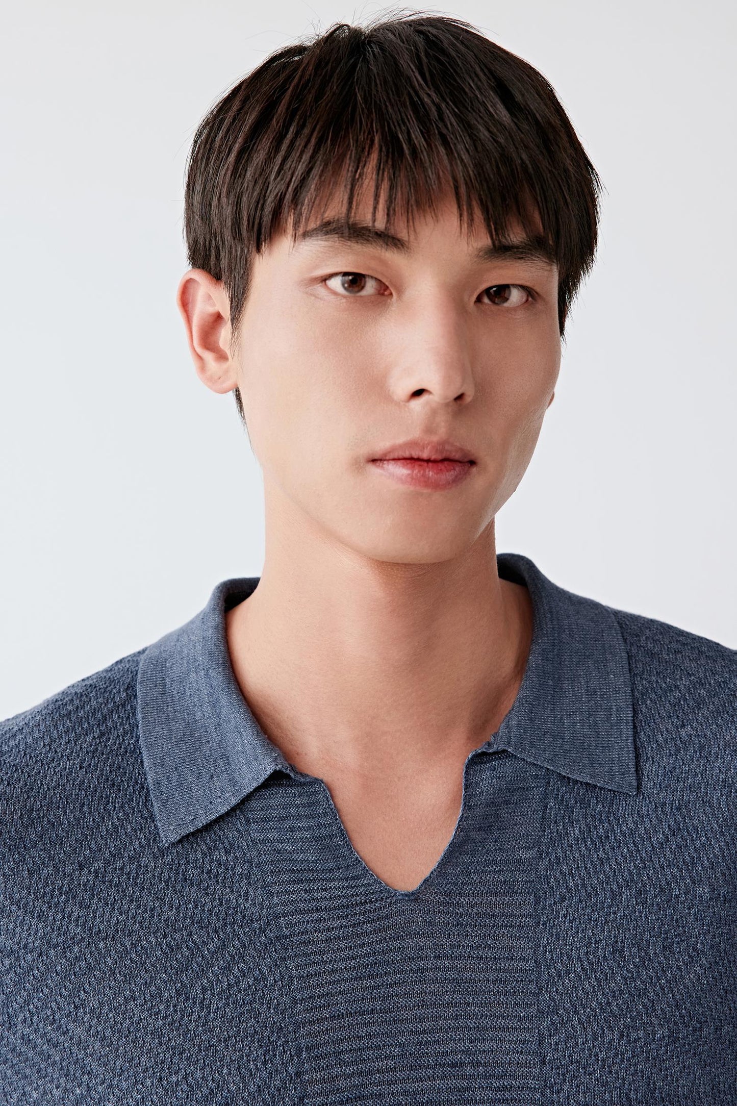 Close-up portrait focusing on the neckline, detailing the soft V opening, ribbed trim and the slightly irregular knit texture, with the blue tone revealing depth and variation in the yarn