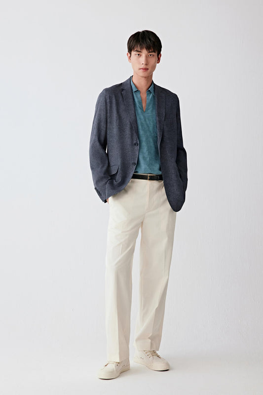 Full-length front view of a man standing facing forward wearing an indigo blue silk twill jacket paired with a teal shirt and light trousers, highlighting the straight silhouette, clean tailoring and fluid drape, with a smooth surface and subtle diagonal twill weave adding depth to the color