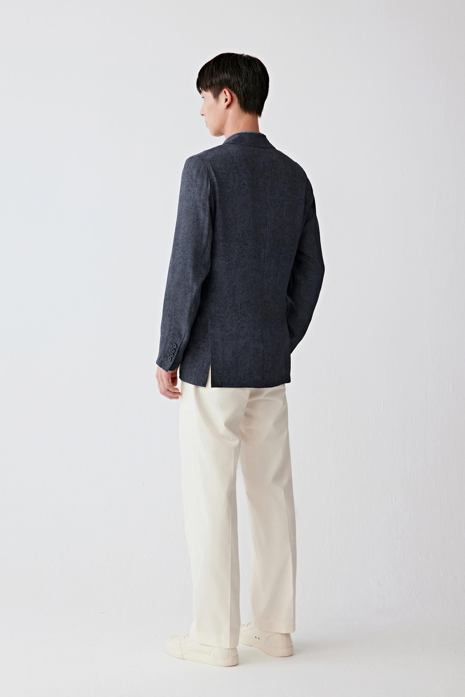 Full-length back view showing the rear silhouette, highlighting the structured shoulders, straight cut and continuous fall from collar to hem, with the fabric maintaining a fluid yet controlled drape