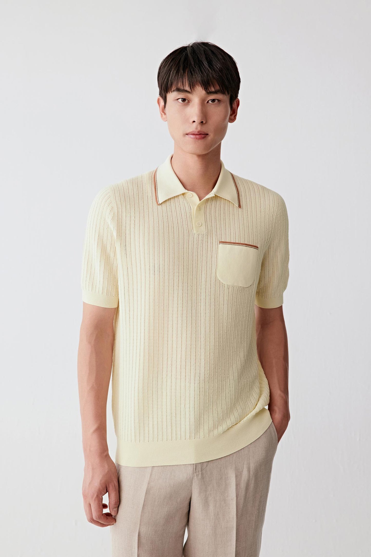 Front view of a man wearing a pale yellow polo shirt in fine cotton knit, highlighting the relaxed silhouette, lightweight knit construction and softly textured surface. The vertical openwork stitch structure creates subtle depth and texture across the fabric while maintaining an even appearance.