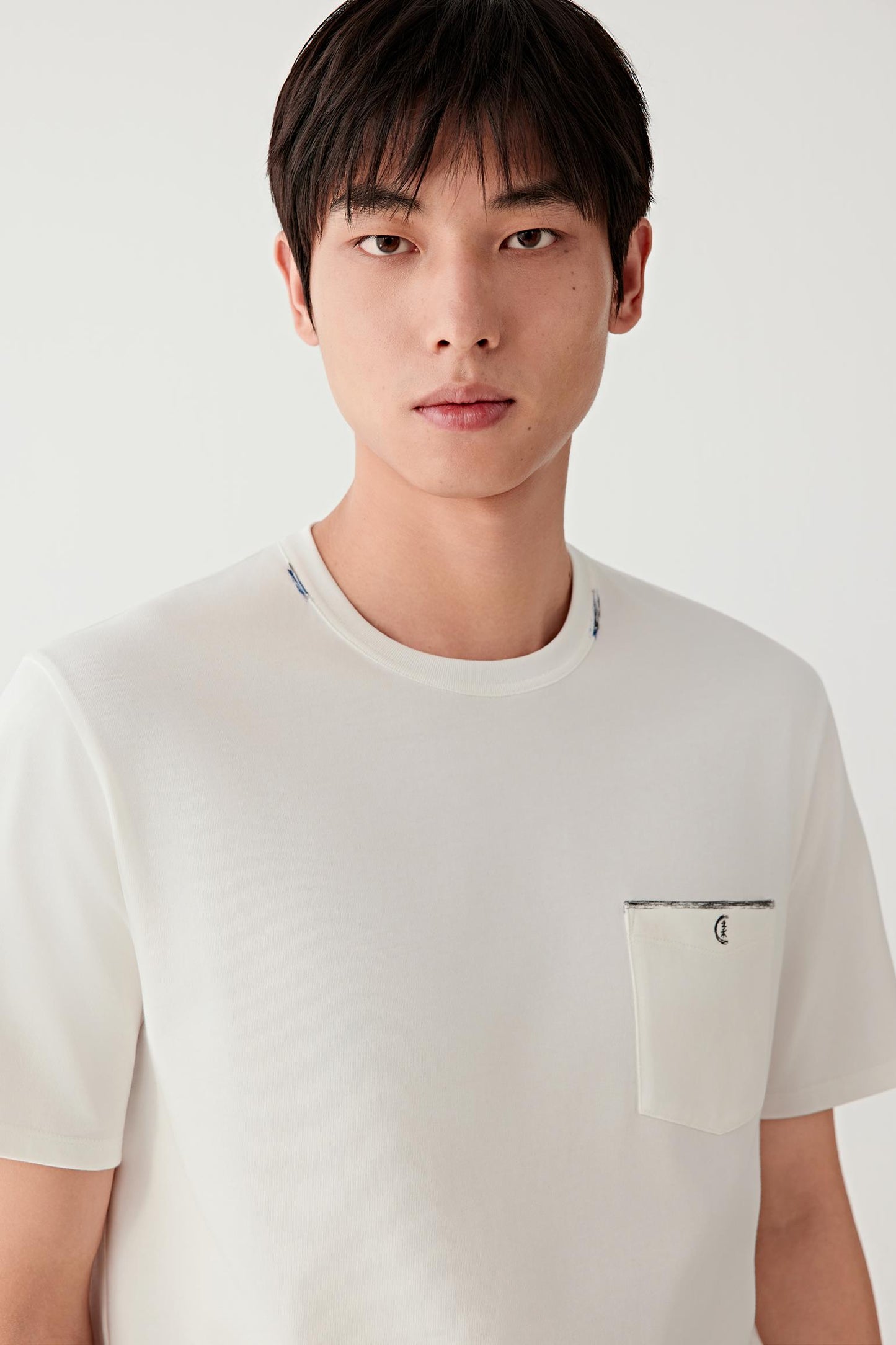 Mid-length front view focusing on the upper body, emphasizing the round neckline, chest pocket with visible stitching and the clean construction, with the white shade enhancing the clarity of lines and structure