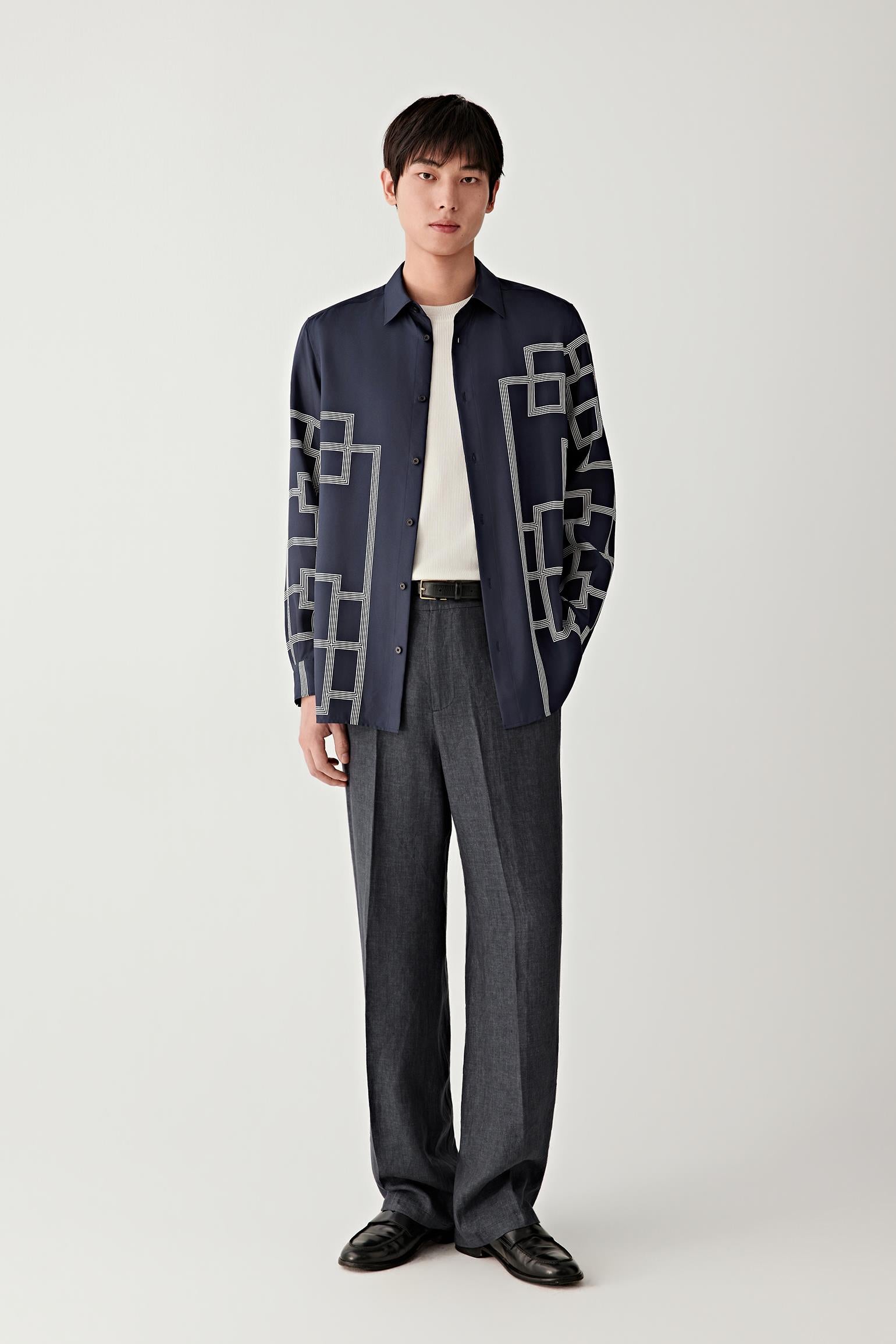 Male model wearing a navy silk twill shirt with geometric white lattice pattern, paired with dark trousers.