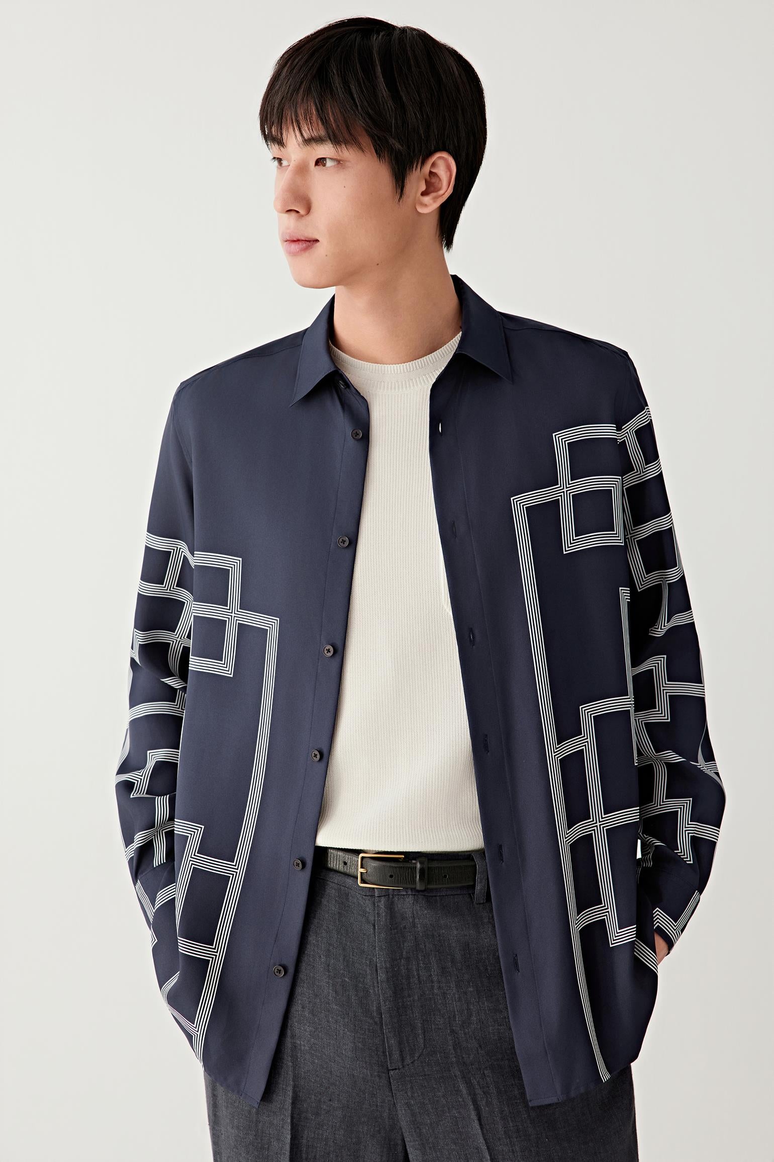 Male model wearing a navy silk twill shirt with geometric white lattice pattern, paired with dark trousers.
