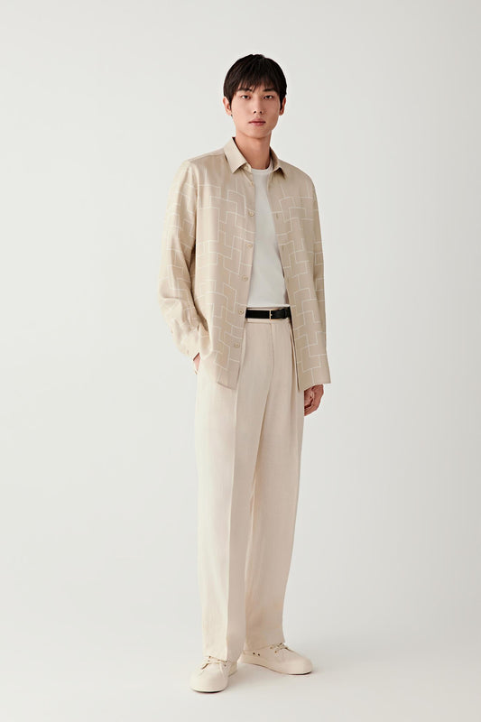 Male model wearing a beige silk twill shirt with subtle white geometric pattern, styled with matching light trousers.