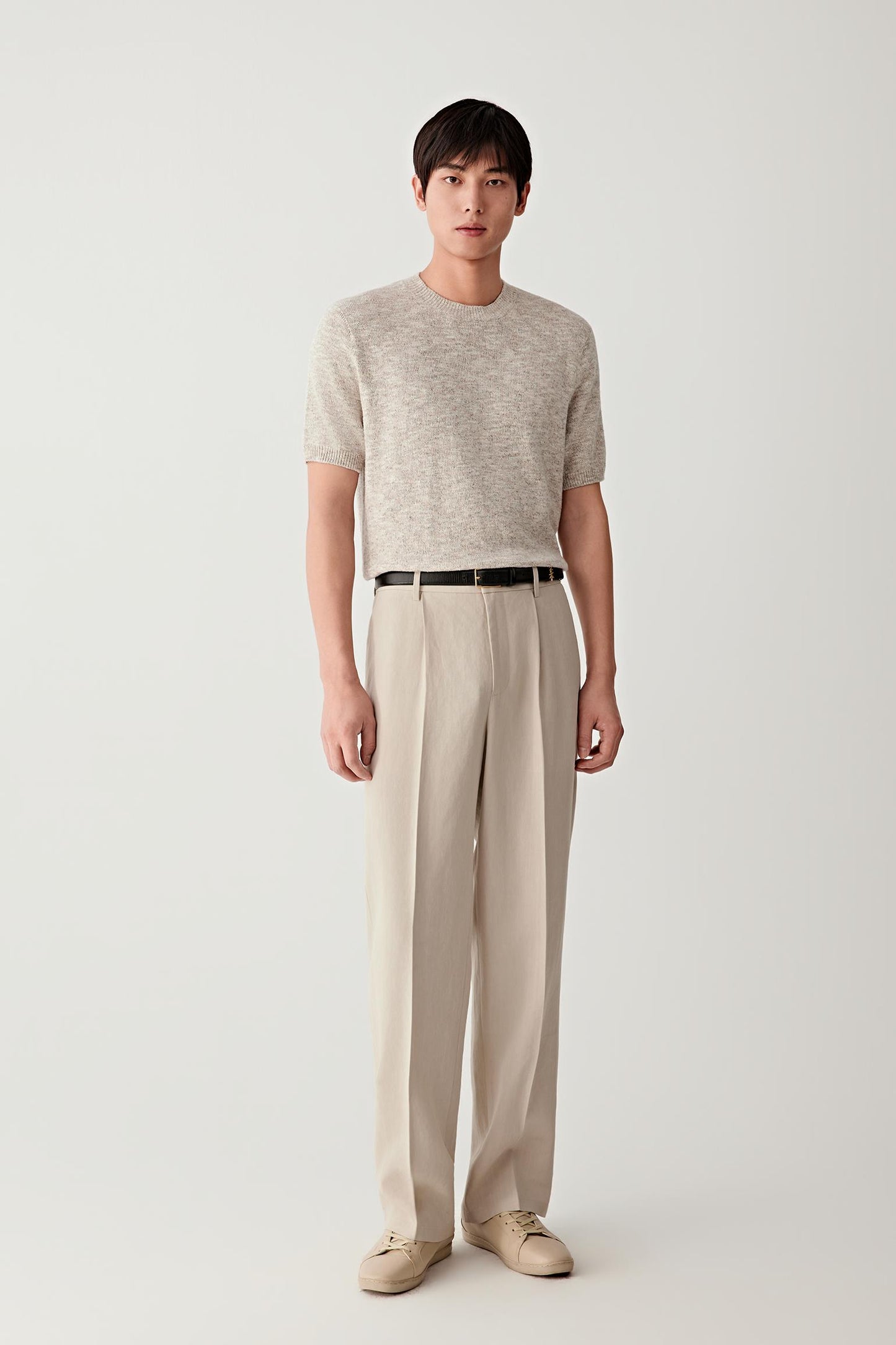 Full-length front view of a beige short-sleeve cotton and silk knit pullover paired with light trousers.