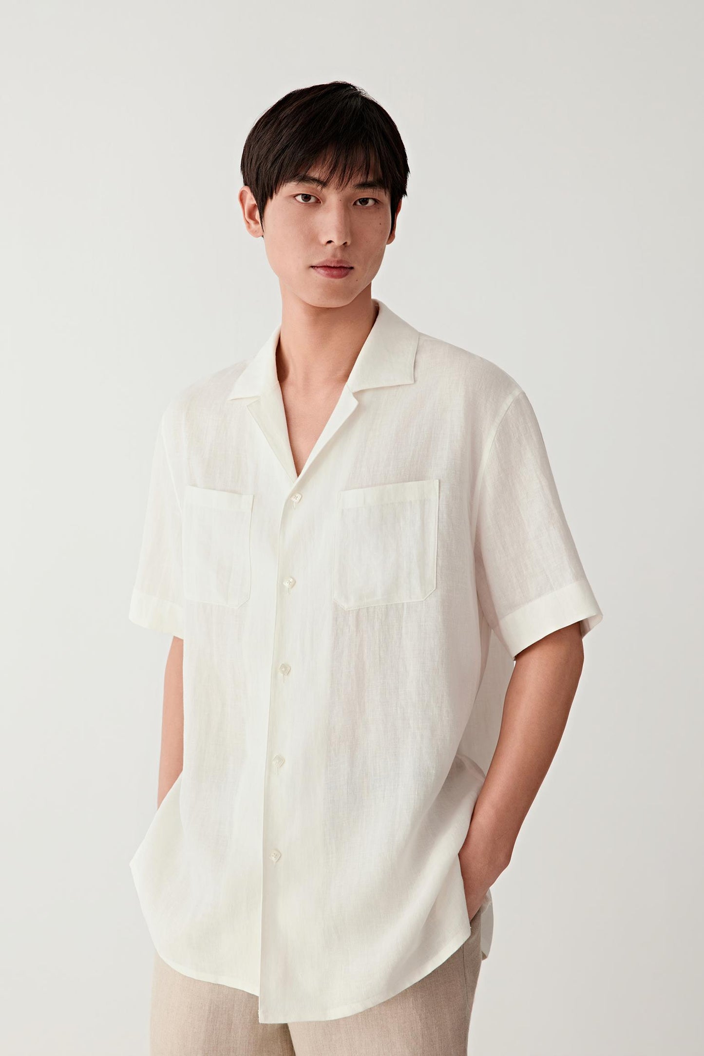 Front view of a man wearing a cream short-sleeved linen shirt, highlighting the relaxed silhouette, lightweight structure and softly textured surface. The natural irregularities of the linen weave create subtle tonal variation across the fabric.