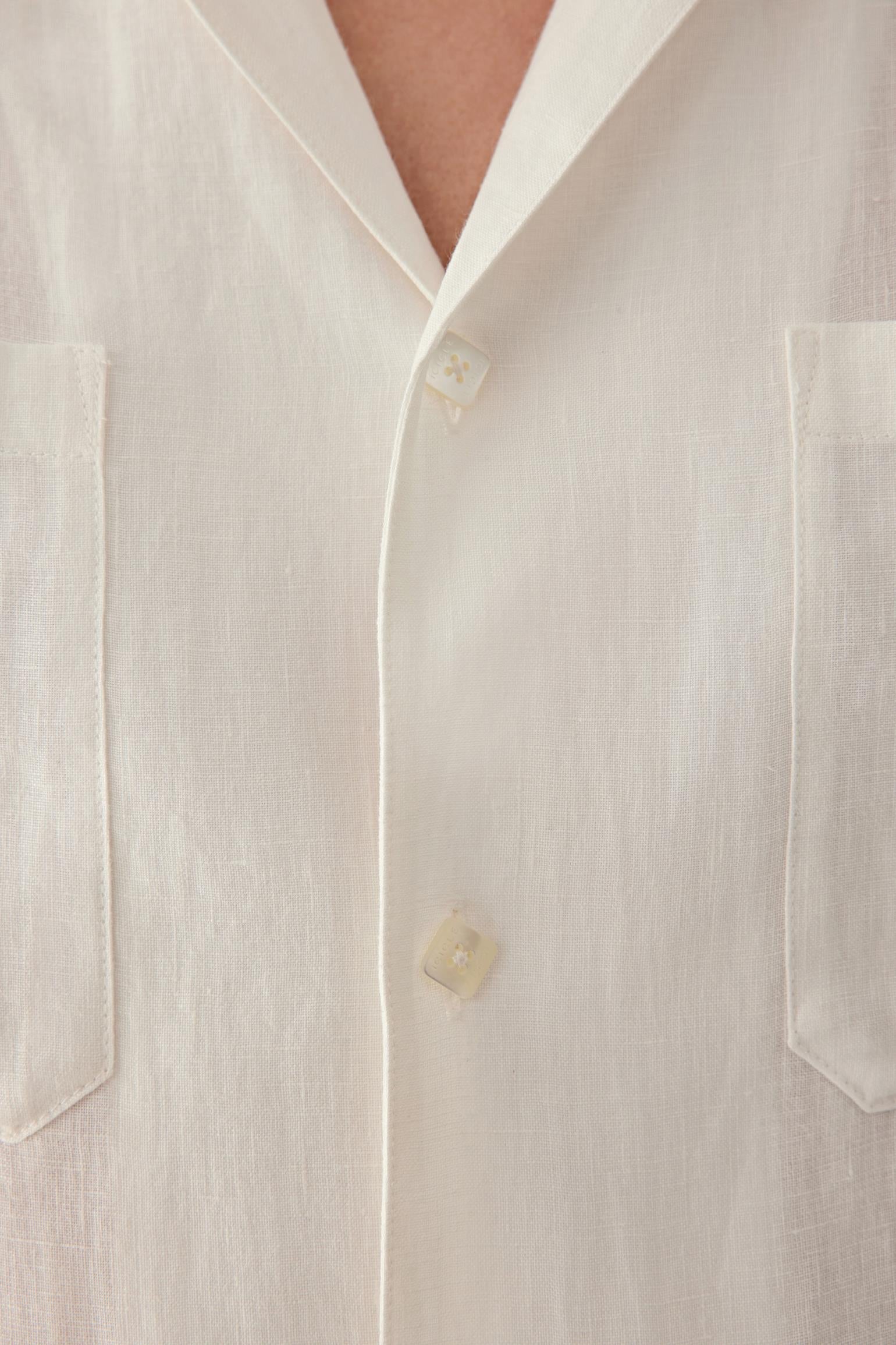 Close-up of the collar and front button fastening, showing the soft structure of the neckline, the natural texture of the linen surface and the subtle tonal depth created by the woven construction.