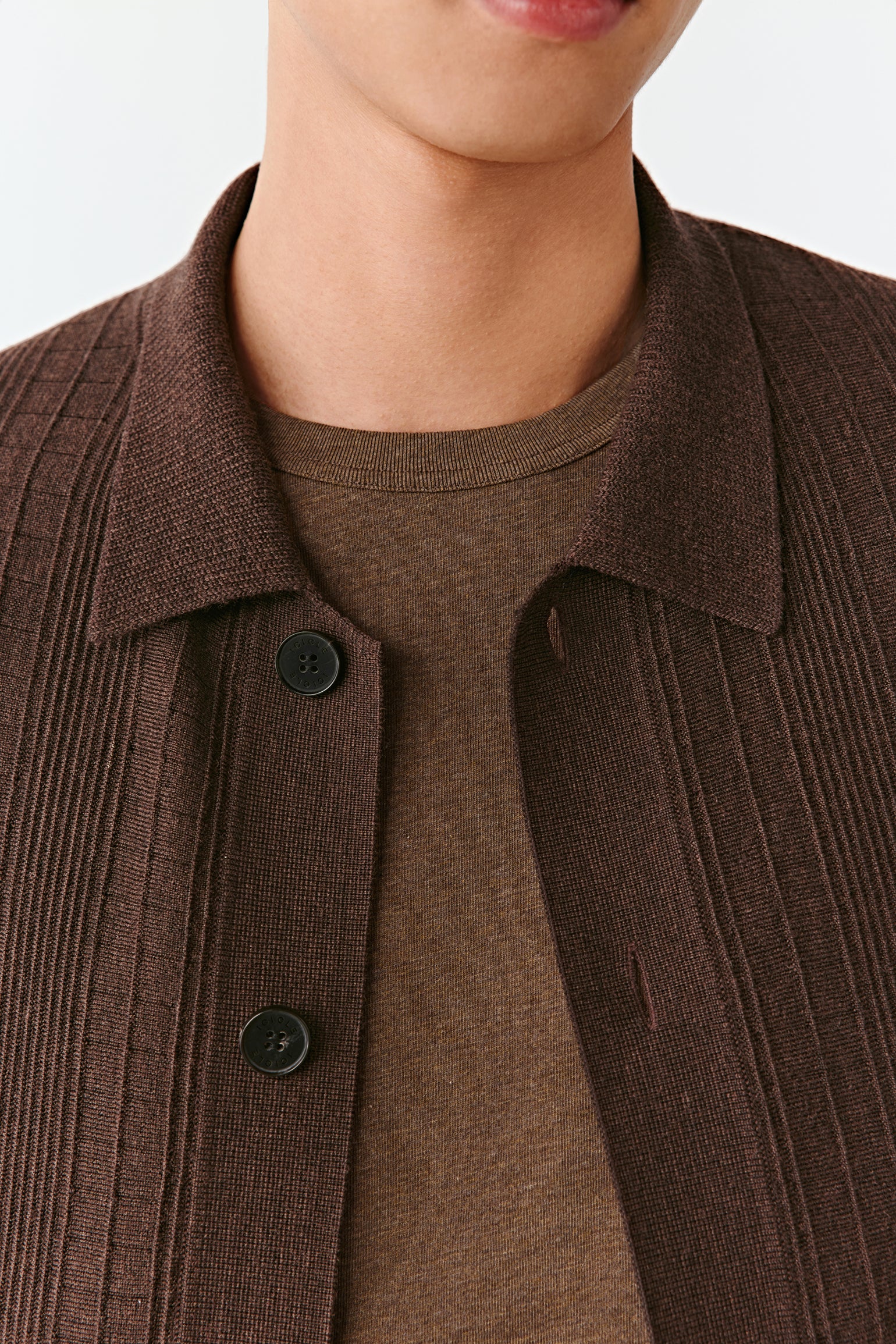 Close-up of a person wearing a brown ribbed sweater with a collar.