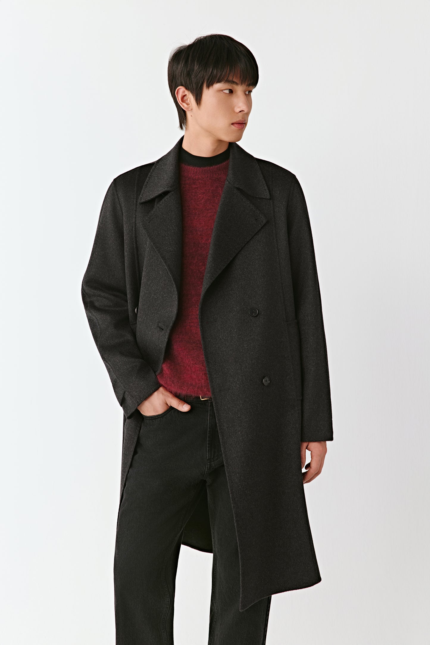 Man wearing a long black coat over a red sweater on a white background