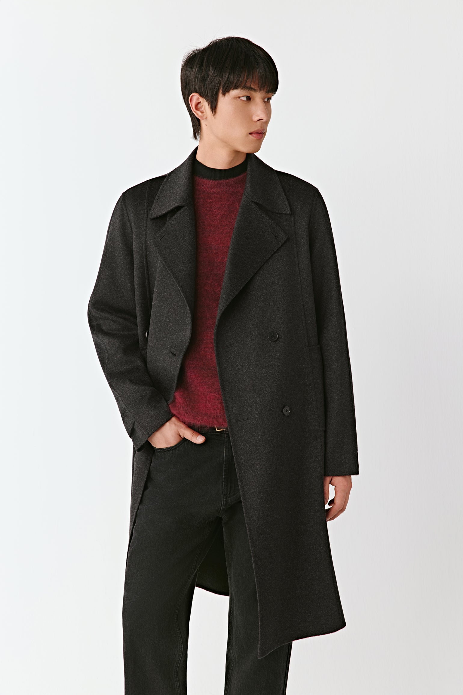 Man wearing a long black coat over a red sweater on a white background