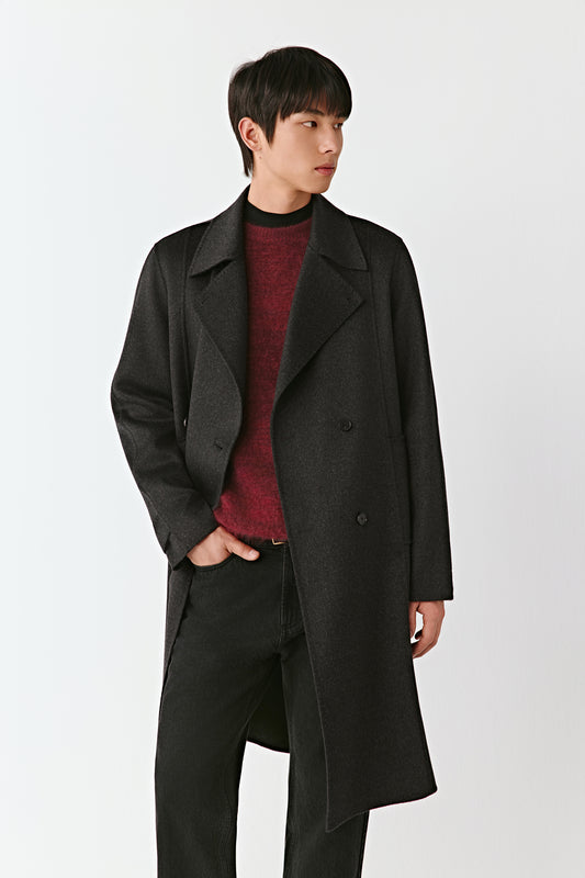 Man wearing a long black coat over a red sweater on a white background