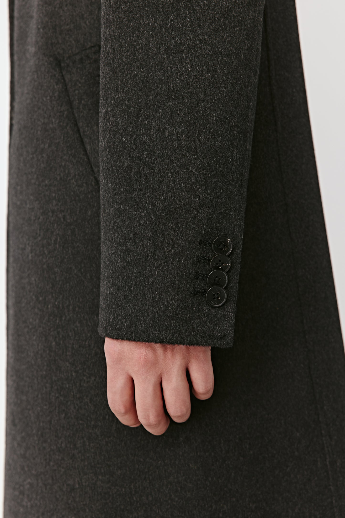 Close-up of a dark grey coat with a buttoned sleeve on a light gray background