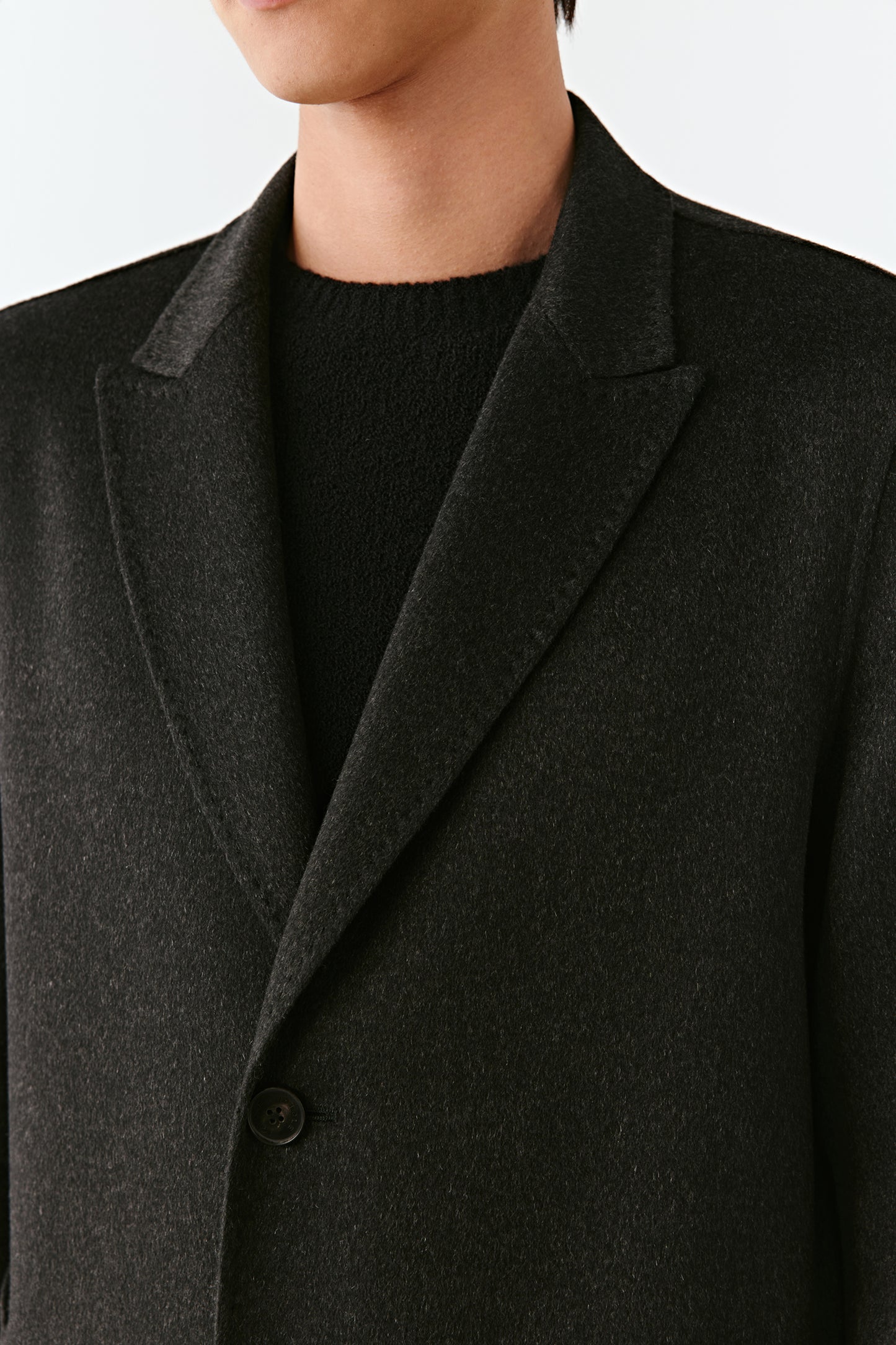 Close up of a black coat worn by a man on a light gray background