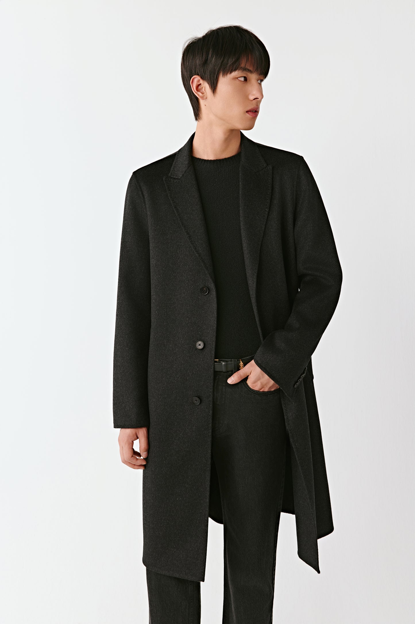 Man wearing a black coat over a black t-shirt and pants on a white background