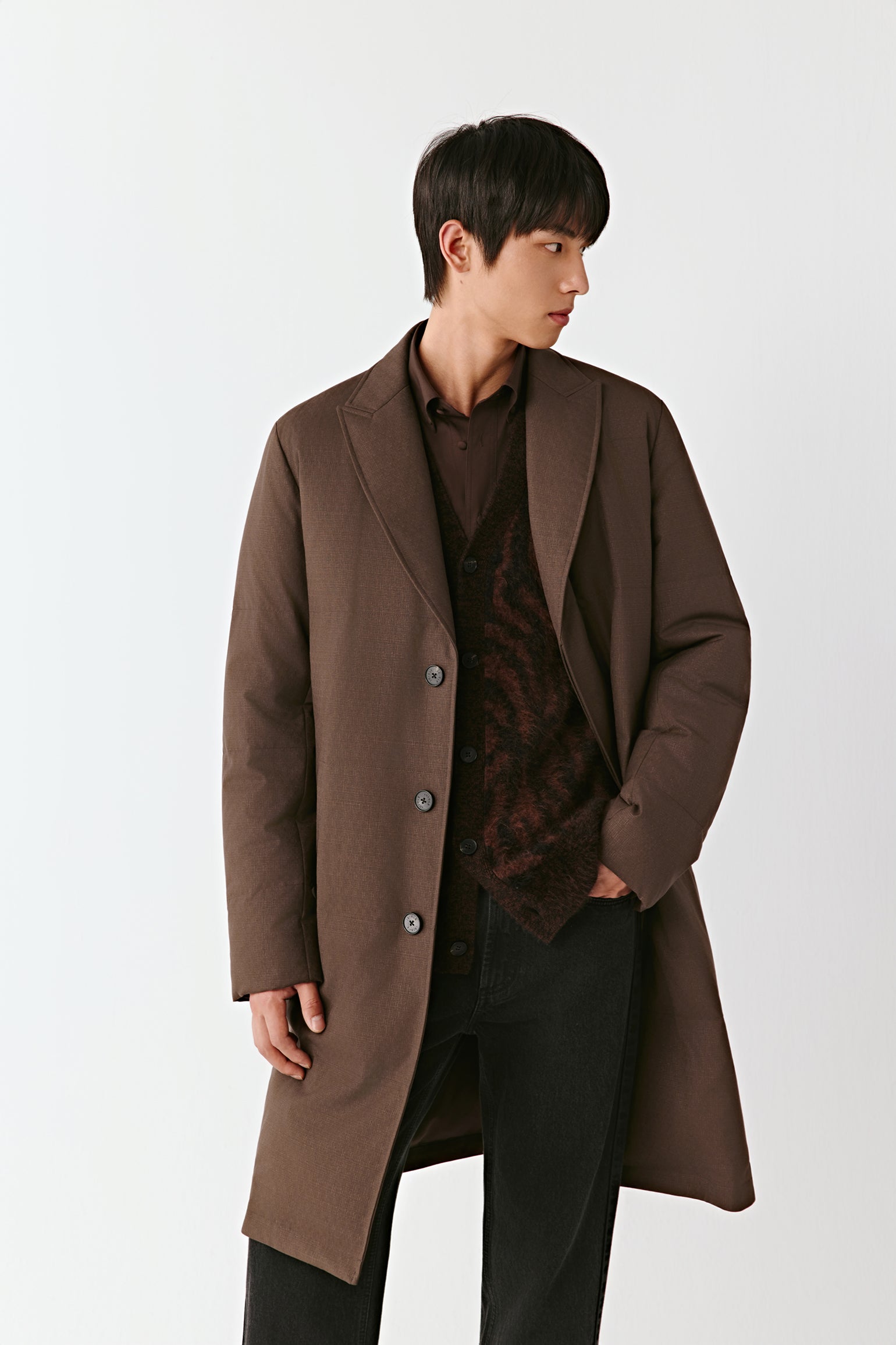 Man wearing a brown coat over a dark shirt on a white background