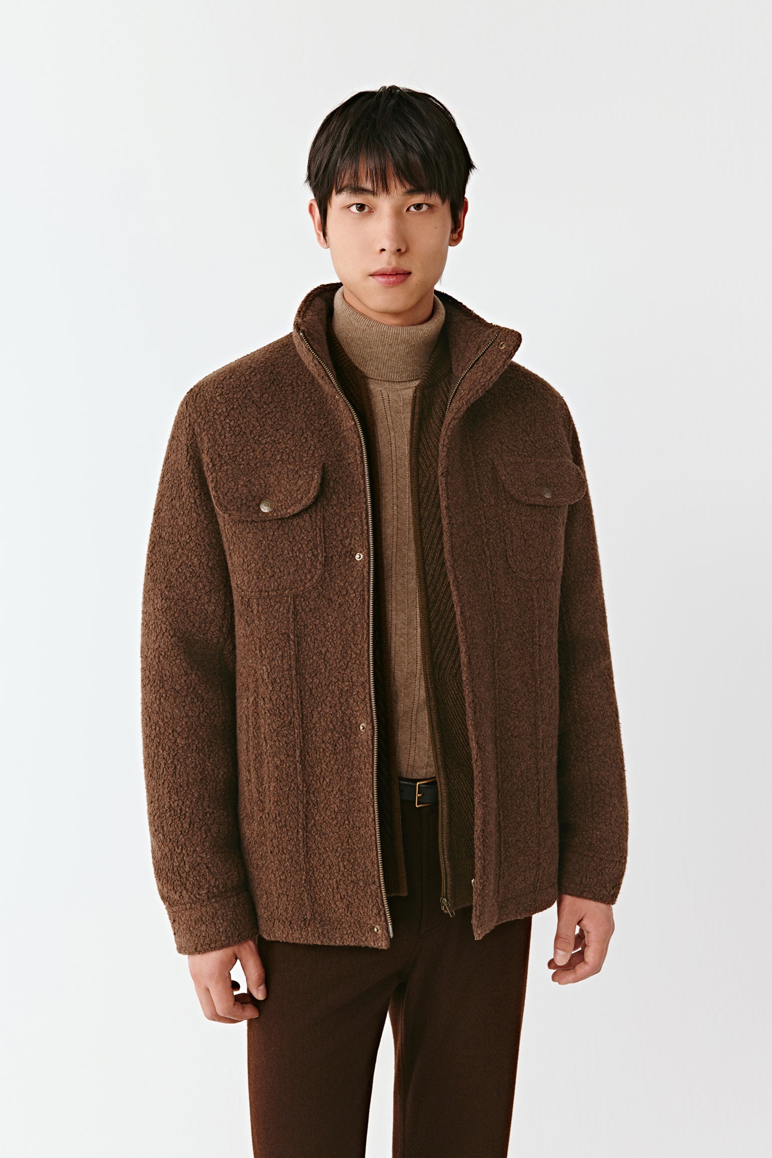 Man wearing a brown jacket over a sweater on a white background