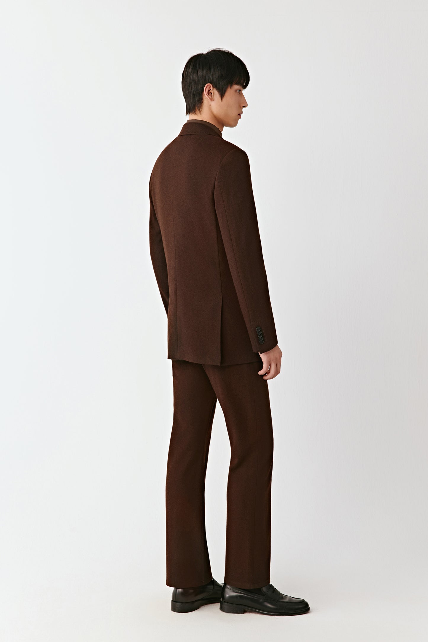 Man wearing a brown suit standing against a white background