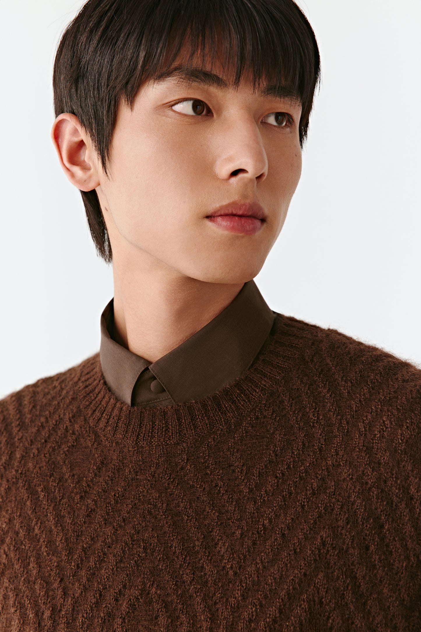 Person wearing a brown sweater and shirt against a plain background