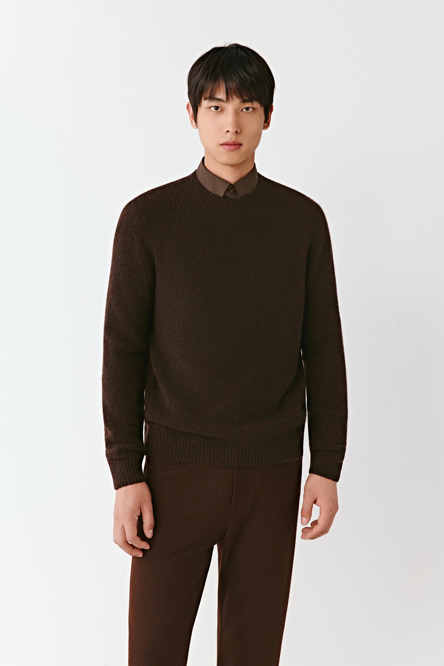 Man wearing a brown sweater and pants on a white background