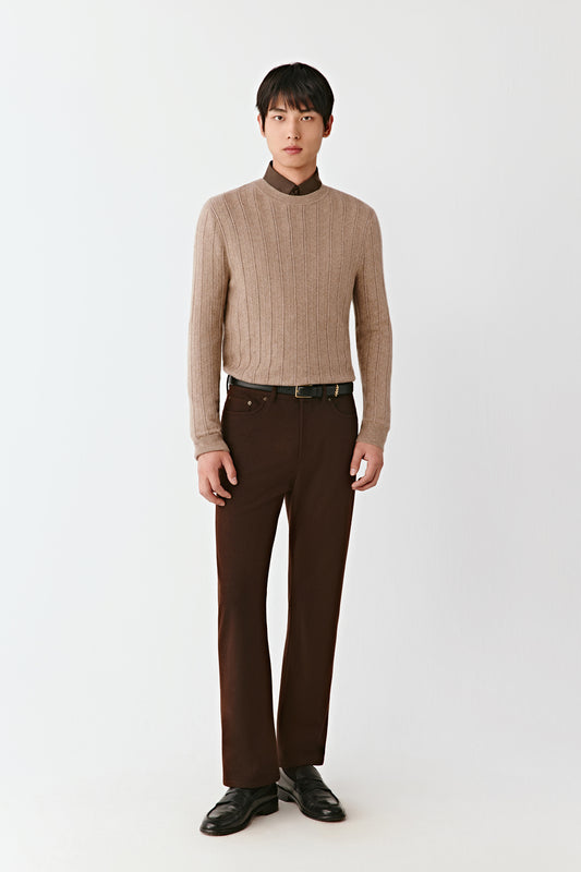 Man wearing a beige sweater and brown pants on a white background