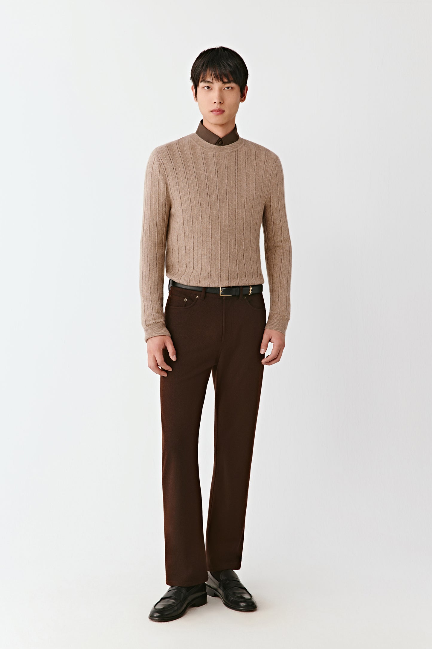Man wearing a beige sweater and brown pants on a white background