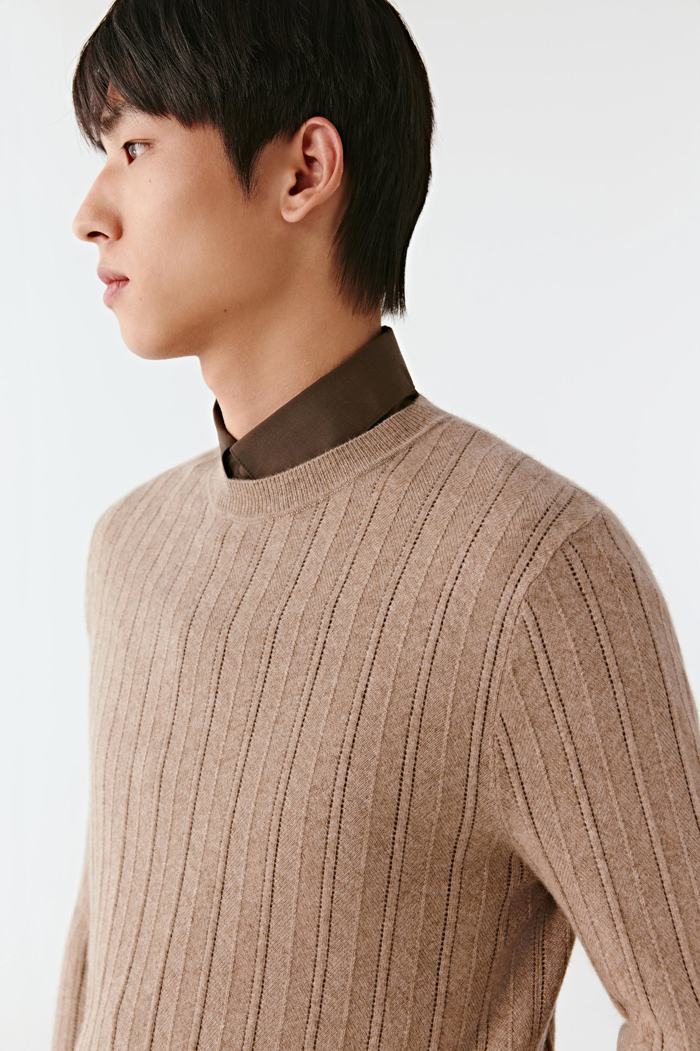 Person wearing a beige ribbed sweater on a white background