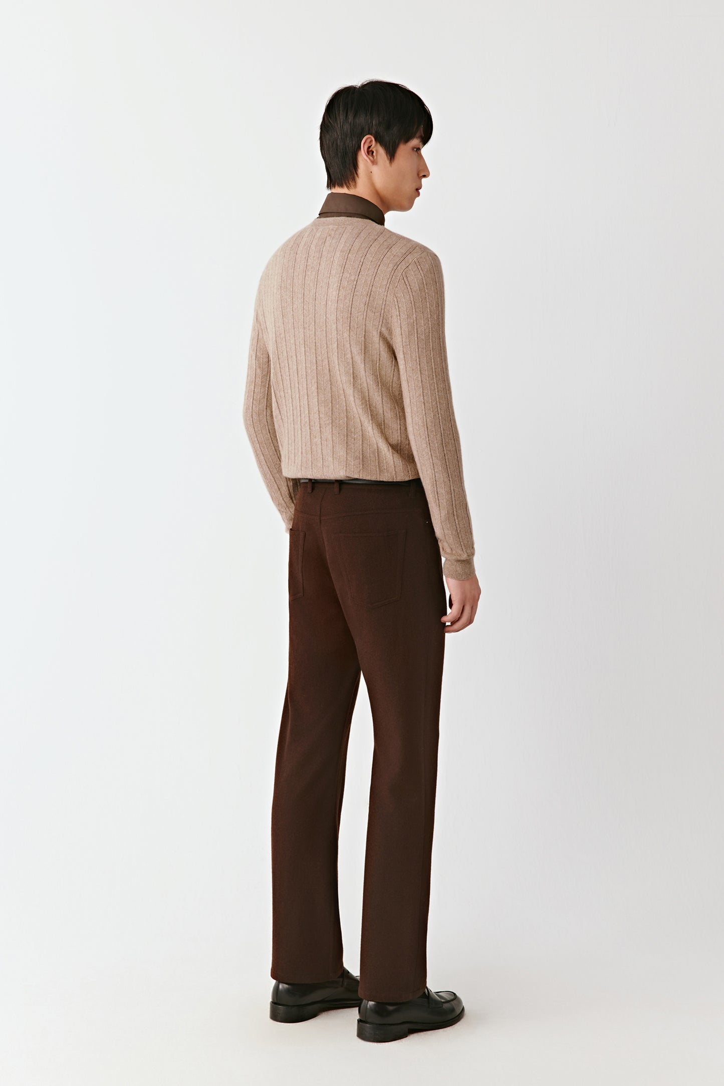 Person wearing a beige ribbed sweater and brown pants on a white background
