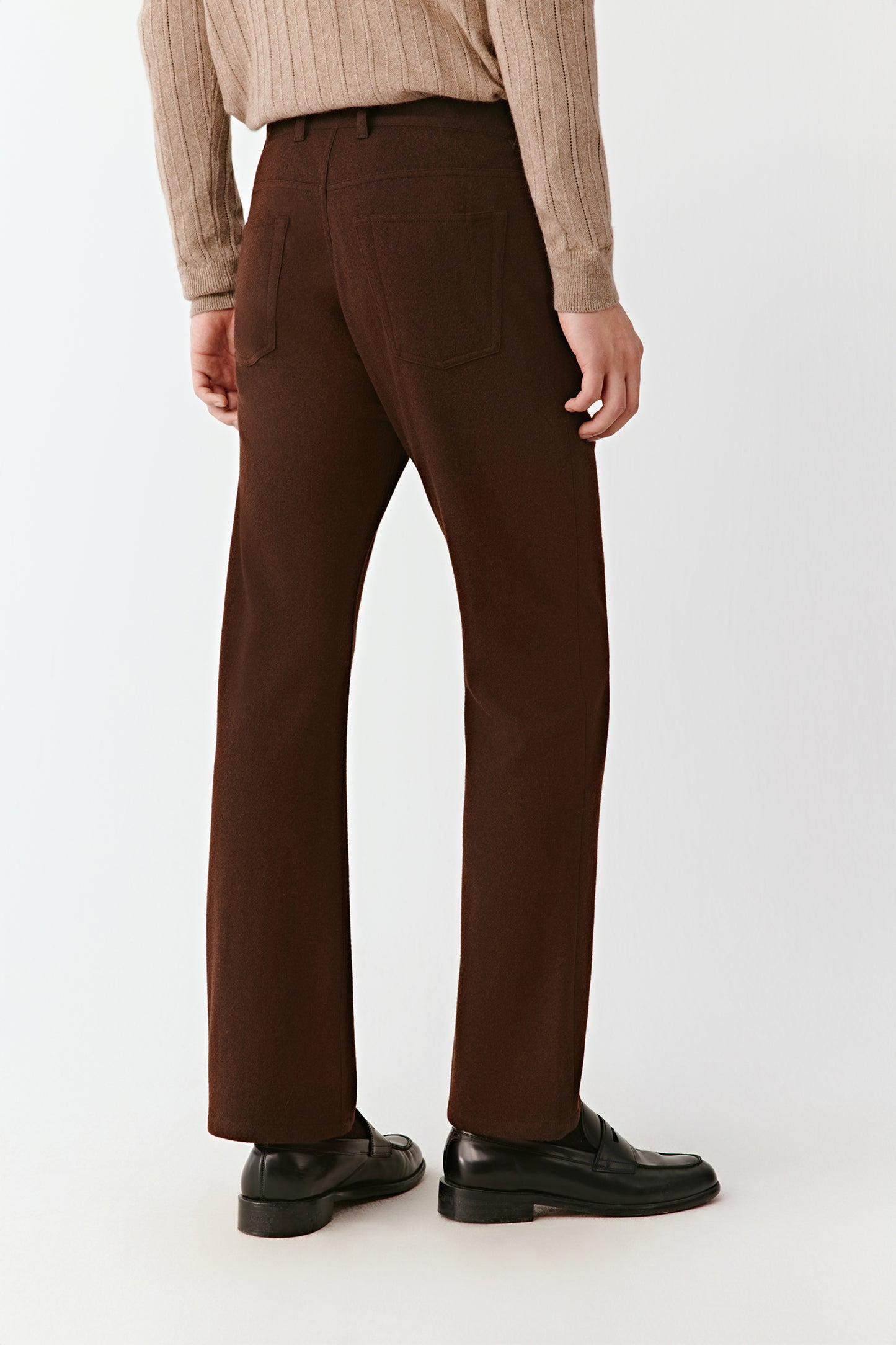 Person wearing brown pants and a beige shirt on a white background