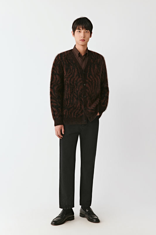 Man wearing a brown patterned cardigan and black pants on a white background