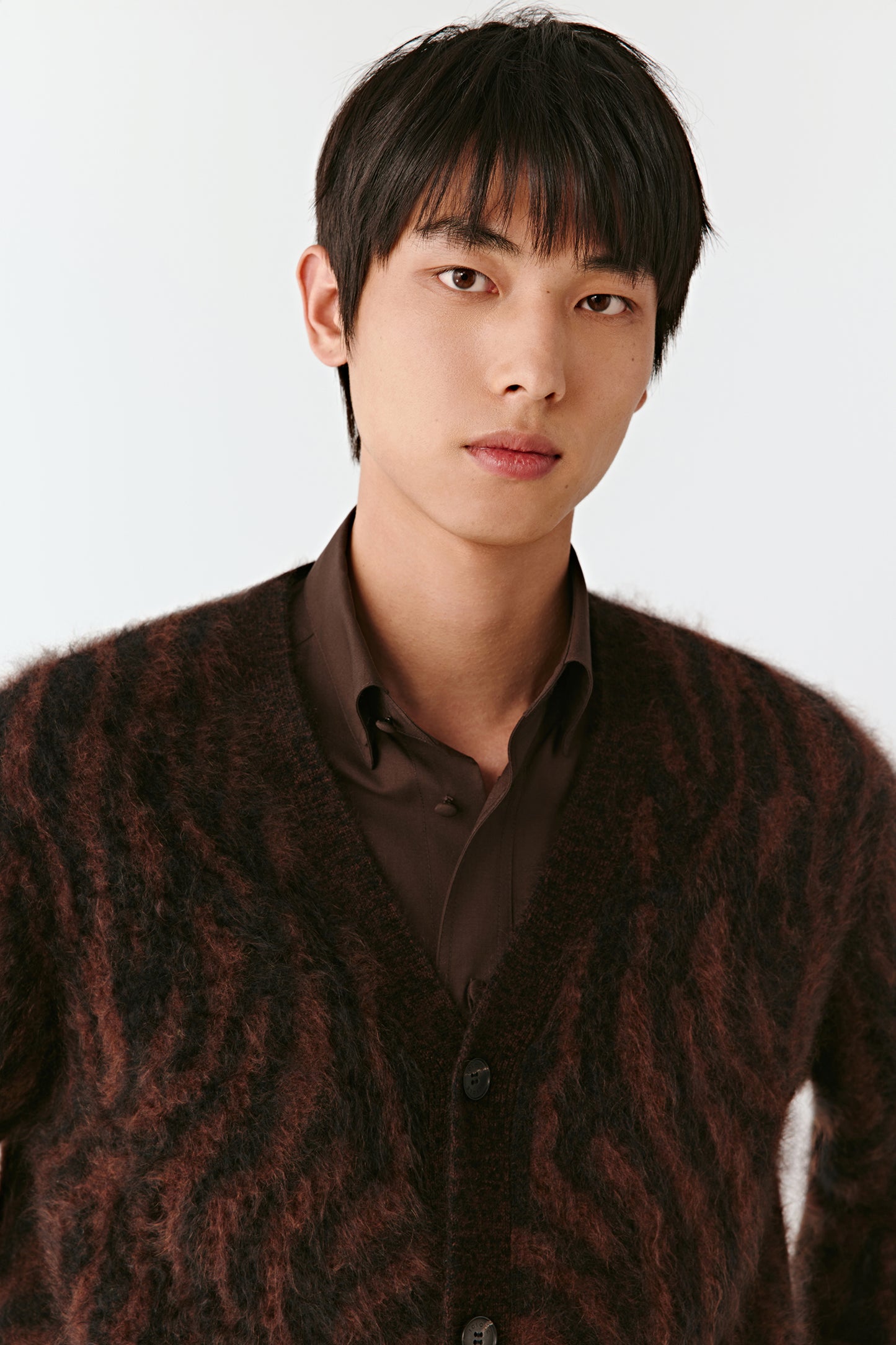 Man wearing a patterned cardigan over a shirt against a white background