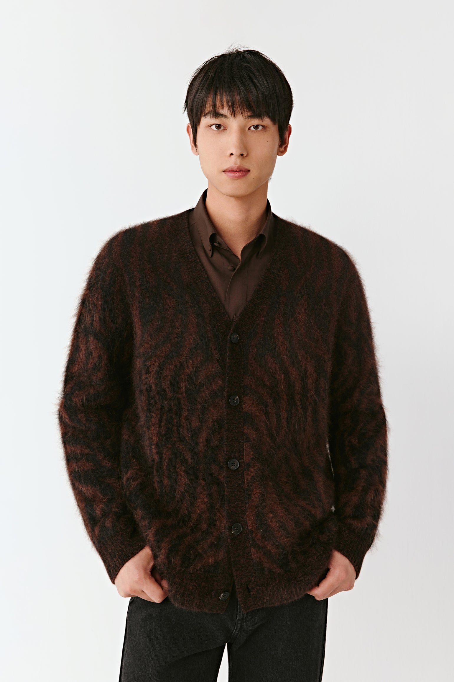 Man wearing a brown patterned cardigan over a shirt on a white background