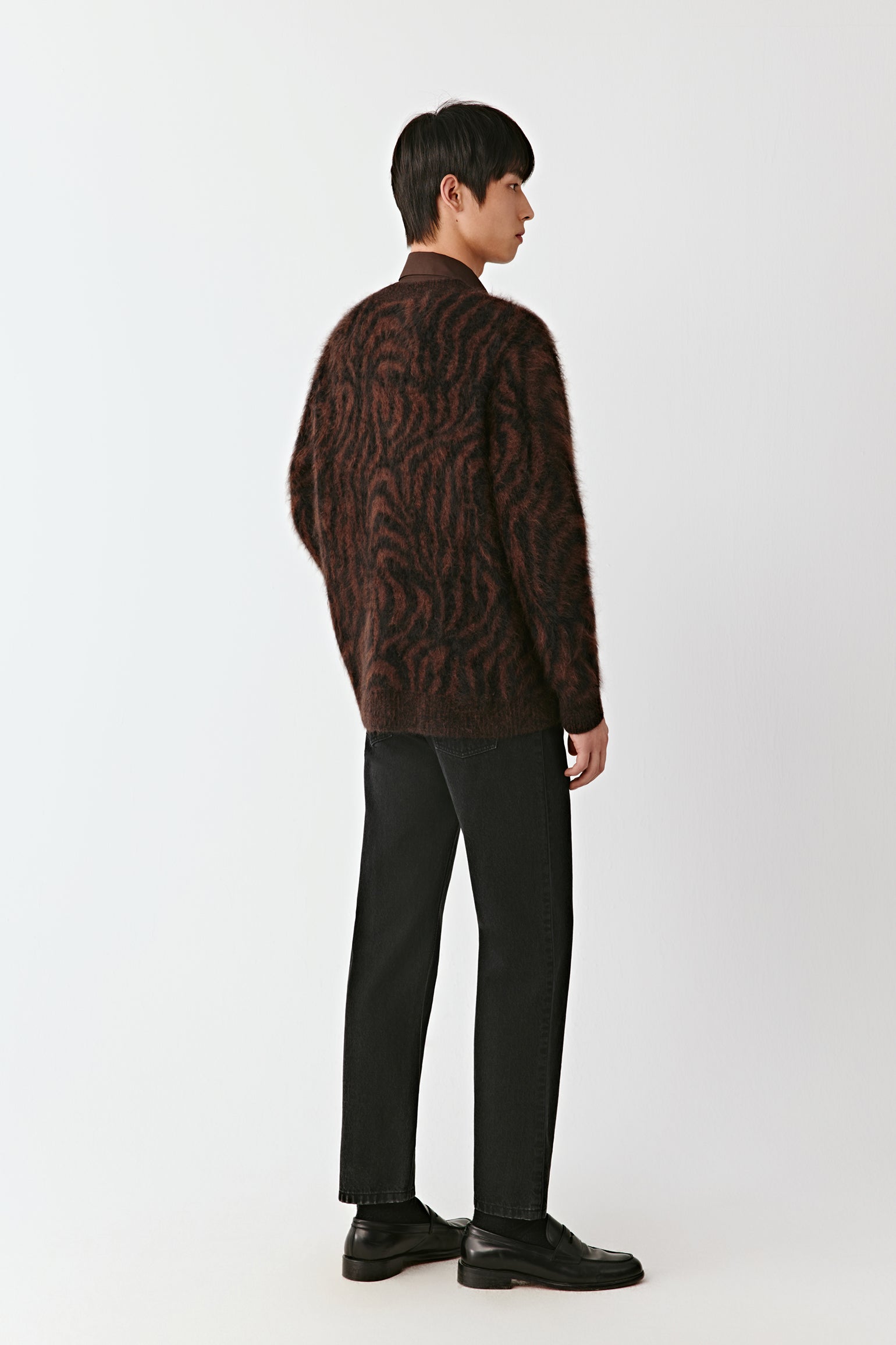 Person wearing a brown patterned cardigan and black pants on a white background