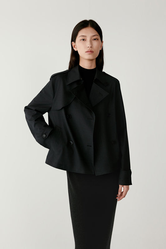 Three-quarter view of the black double-breasted jacket showing the wide lapel collar, the double row of front buttons and the slightly boxy tailored silhouette. The jacket’s hip-length cut and long sleeves are clearly visible.
