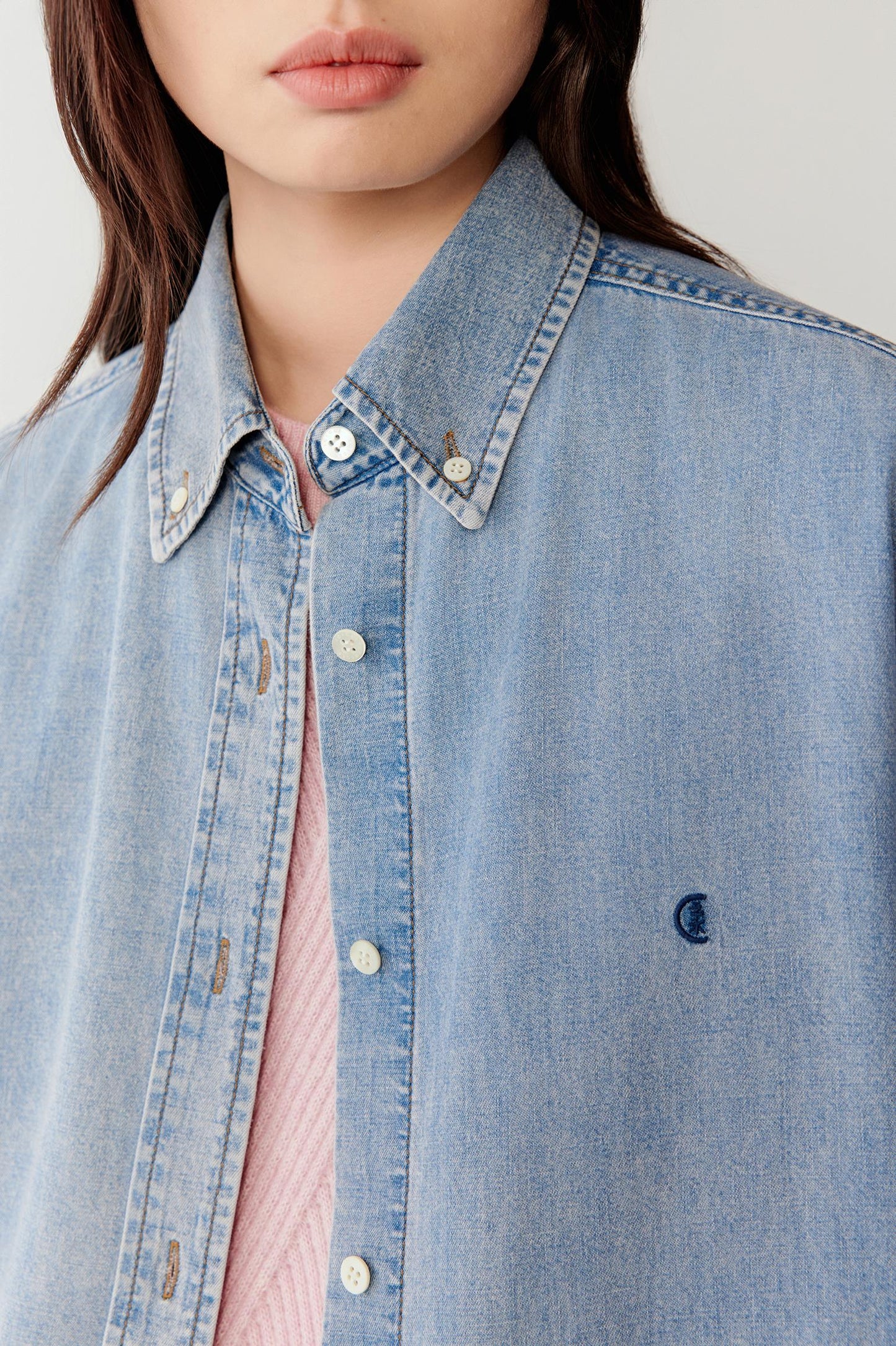 Close-up front view of collar and upper chest showing the light blue washed denim, visible stitching, button placket and soft, slightly textured surface