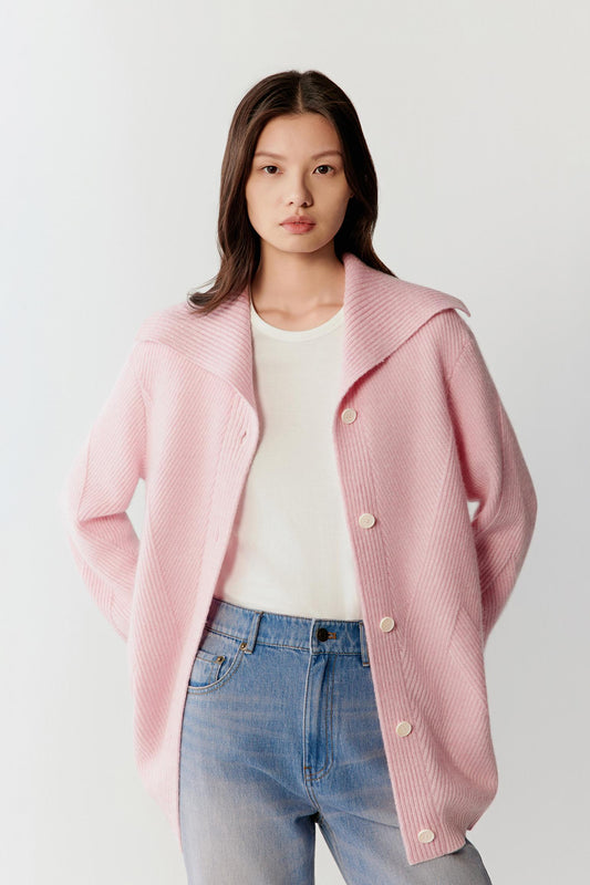 Female model wearing a pink melange buttoned cardigan over a white top and blue jeans.