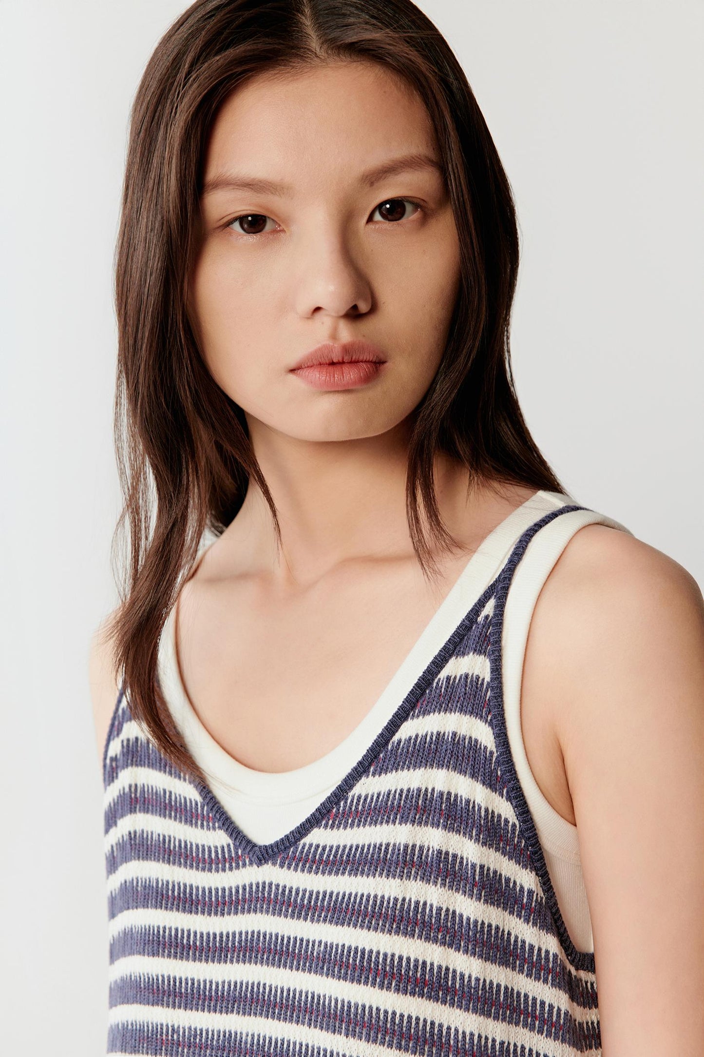 Close-up portrait focusing on the neckline and upper body, detailing the softly curved neckline, fine straps and subtly textured striped knit surface